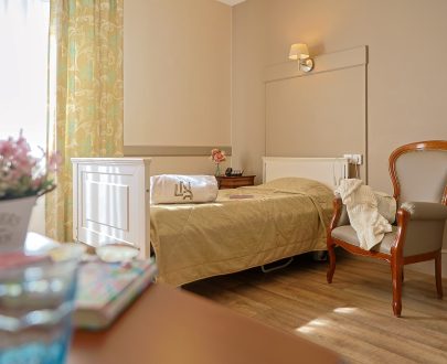 Chambre Asphodia décorée avec lit simple médicalisé, fauteuils et grande fenêtre
